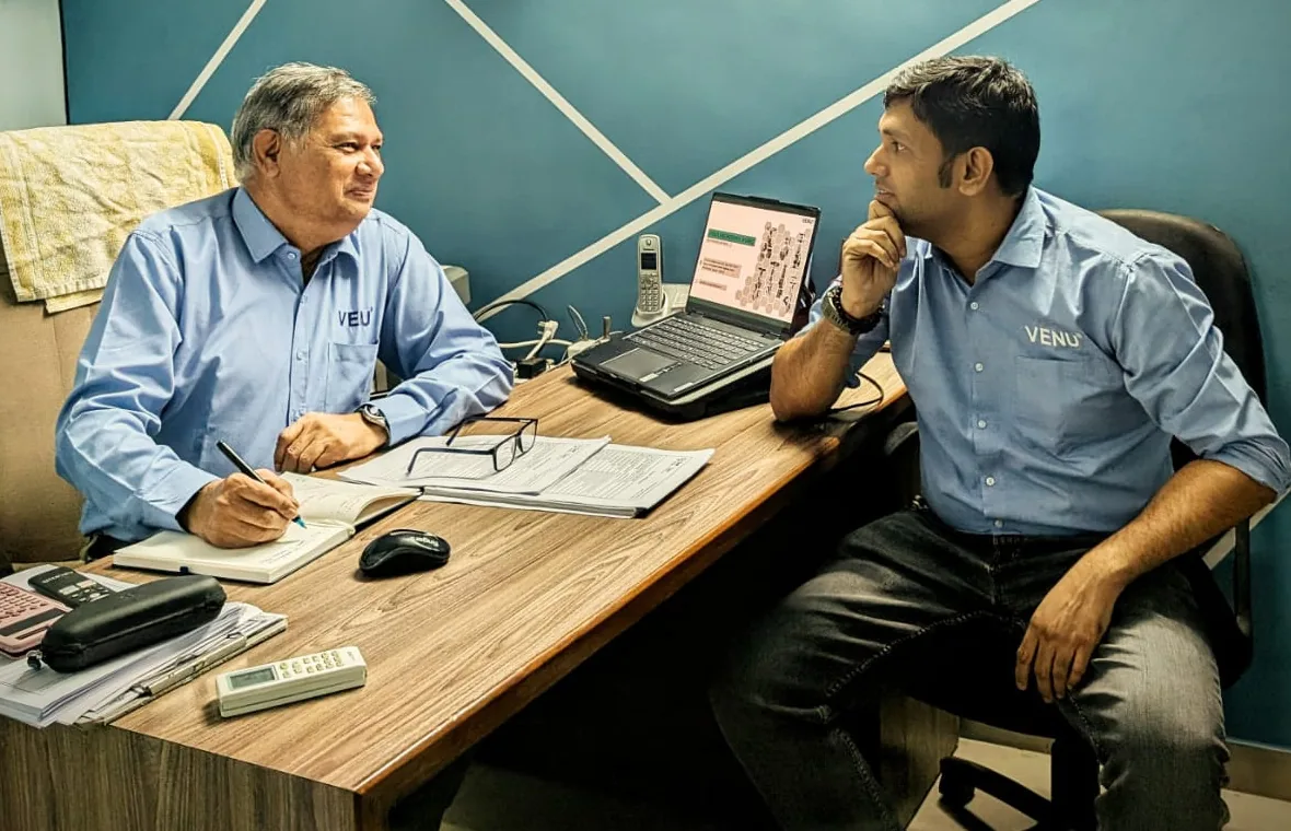 Mr Anand Mashruwala and Mr Anay Mashruwala seated either side of a desk at the Ahmedabad works, drawings and a laptop between them.