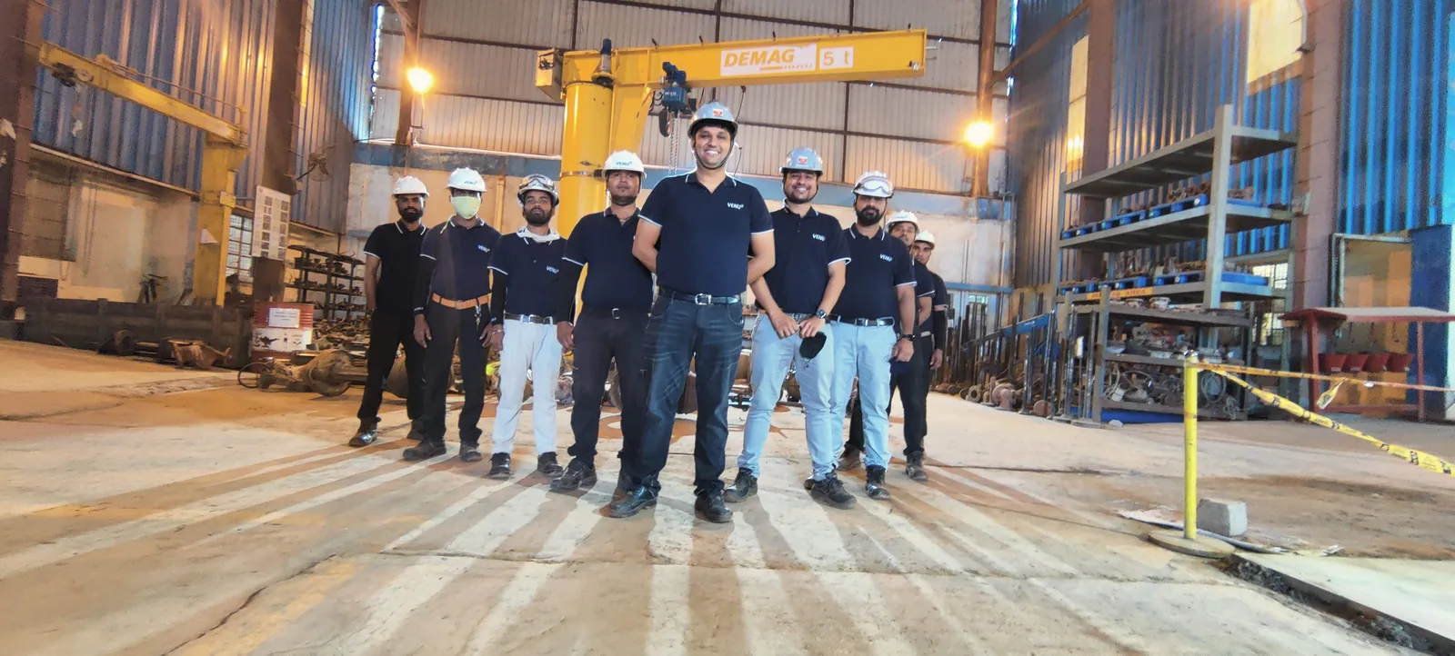 Nine members of the shop-floor team in Venus polo shirts and hard hats, standing beneath the overhead crane at the Kuha works.