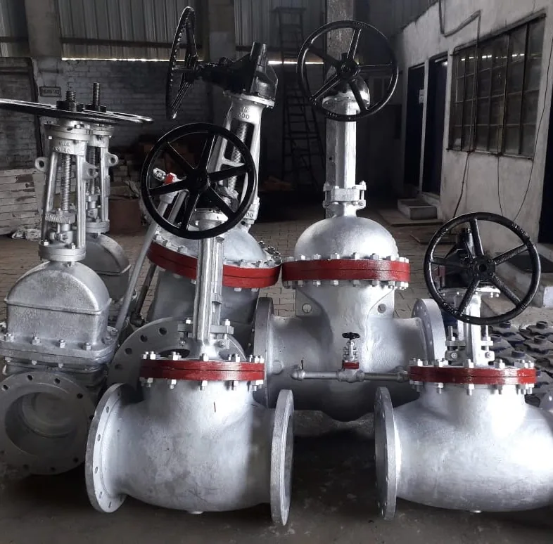 A row of large cast steel gate and globe valves with handwheels and red-painted flange faces, standing on the shop floor.